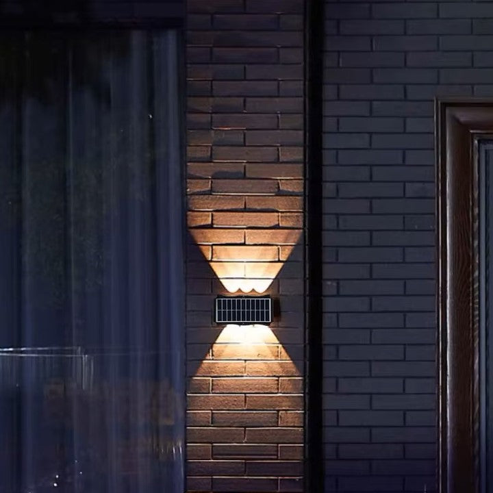 Une-applique-solaire-exterieur-prise-en-photo-chez-le-voisin-à-travers-une-vitre.-Elle-est-installé-sur-un-mur-de-brique.